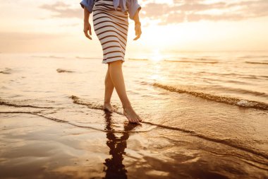 Yakın plan, genç bir kadının yaz plajında deniz suyu ve kum dalgası boyunca yürümesi. Seksi, zayıf ve bronzlaşmış bacaklar. Yaz tatili.