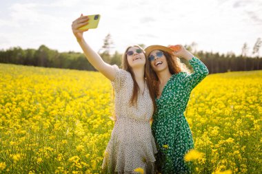 Selfie zamanı. Çiçek tarlasında yürürken iki genç kadın selfie çekiyor. Doğa, tatil, rahatlama ve yaşam tarzı. Yaz manzarası.