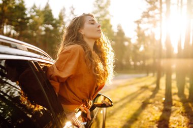 Güzel gezgin kadın dinleniyor ve gün batımının tadını çıkarıyor. Yaz gezisinde mutlu bir kadın, araba camından sarkıyor. Aktif yaşam tarzı, turizm. Seyahat kavramı.