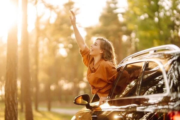 美丽的女旅行家正在休息 欣赏着车上的落日 一个快乐的女人在夏天的旅行中 靠着车窗去旅行 积极的生活方式 旅行概念 — 图库照片