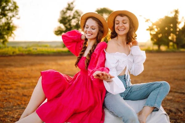 日落时 两个漂亮的女人在草堆里玩得很开心 戴着帽子的时髦姑娘们在战场上玩得很开心 生活方式和娱乐的概念 — 图库照片