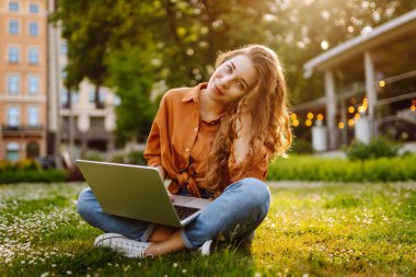 Güzel kadın serbest yazar elinde dizüstü bilgisayarla yeşil bir çayırda oturuyor. Online eğitim. Güneşin tadını çıkaran mutlu bir kadın. Bağımsız kavram.