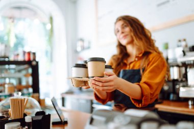 Senin için en iyi kahve. Barda önlüklü neşeli bir kadın bir kafede kahve bardakları tutuyor. Paket yemek konsepti.