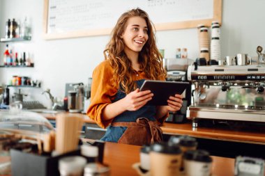 Güzel kadın bir kahve dükkanının arkasında duruyor. Dijital tabletli bir barista sipariş alır. İş konsepti. Paket yemek..