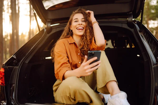 Piękna Kobieta Siedzi Bagażniku Samochodu Lesie Używa Smartfona Koncepcja Podróżowania — Zdjęcie stockowe