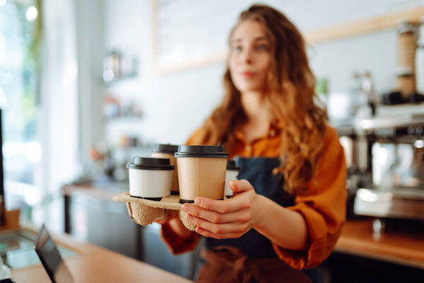 Best coffee for you. Cheerful woman in an apron at the bar counter holds coffee glasses in a cafe. Takeaway food concept.