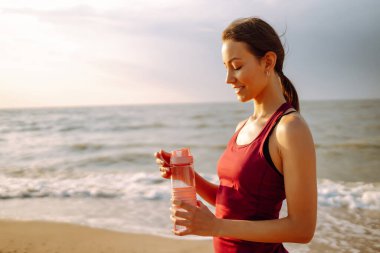 Spor giyimli güzel bir kadın vahşi sahilde yoga minderinde tek başına esneme egzersizi yapıyor. Sağlıklı yaşam tarzı kavramı