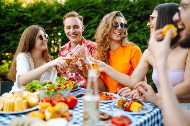 Neşeli genç arkadaşlar dışarıda parti yapıyorlar, konuşuyorlar, bira içiyorlar ve arkadaşlığın tadını çıkarıyorlar. Tatil, piknik, hafta sonu, doğa.