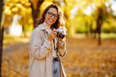 Güz ormanında fotoğraf çeken güzel bir kadın. Sonbahar havasının tadını çıkaran gülümseyen bir kadın. Dinlenme, rahatlama, turizm, yaşam tarzı konsepti.