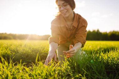 Buğday tarlasında deneyimli çiftçi kadın buğday filizlerini inceliyor. Gülümseyen çiftçi elinde dijital tabletle buğday tarlasının kalitesini kontrol ediyor. Buğday tarlasının ilerleyişini kontrol ediyorum. Tarım kavramı.