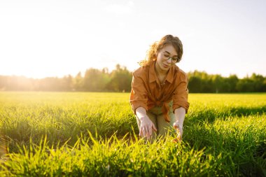 Buğday tarlasında deneyimli çiftçi kadın buğday filizlerini inceliyor. Gülümseyen çiftçi elinde dijital tabletle buğday tarlasının kalitesini kontrol ediyor. Buğday tarlasının ilerleyişini kontrol ediyorum. Tarım kavramı.