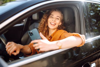 Sürücü koltuğundaki arabada oturan mutlu kadın akıllı telefona bakıyor. Genç bir kadın şehirde yön bulmak ve park ücretini ödemek için cep telefonu kullanıyor. İş, teknoloji kavramı.