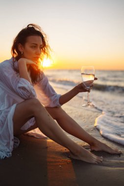 Sıska beyaz elbiseli genç kadın deniz kıyısında gün batımının tadını çıkarıyor. Yaz zamanı. Seyahat, hafta sonu, güneşli, eğlenceli, pozitif ruh hali. Etkin yaşam biçimi.