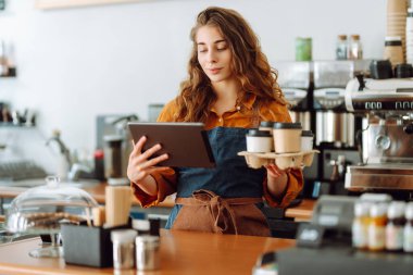 Kıvırcık saçlı ve elinde tablet olan bir kahve dükkanının yakışıklı genç müdürü kahve dükkanında paket kahve veriyor. Paket yemek. İş konsepti.