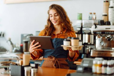 Kıvırcık saçlı ve elinde tablet olan bir kahve dükkanının yakışıklı genç müdürü kahve dükkanında paket kahve veriyor. Paket yemek. İş konsepti.