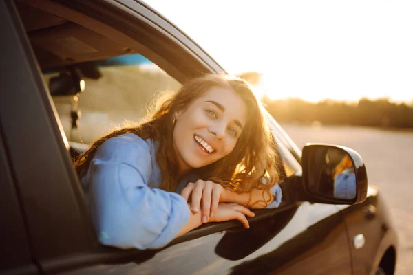 美丽的年轻女子在旅行中欣赏着车窗上的落日 汽车旅行 积极的生活方式概念 日落光 — 图库照片