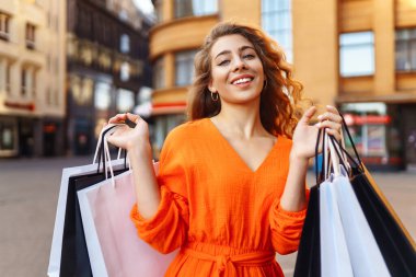 Şehirdeki alışveriş torbaları ve indirimlerden memnun olan şık genç bir kadın. Gülümseyen ve alışveriş yapan mutlu turist kadın Avrupa 'nın güneşli caddelerinde yürüyor. Yaşam tarzı kavramı.