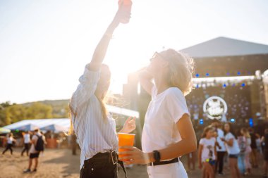 Neşeli iki genç kız arkadaş plaj partisinde birayla eğleniyor. Mutlu iki kadın müzik festivalinde hafta sonunun tadını çıkarıyor. Arkadaşlık, tatil, hafta sonu kavramı..