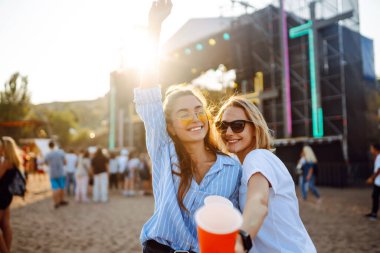 Neşeli iki genç kız arkadaş plaj partisinde birayla eğleniyor. Mutlu iki kadın müzik festivalinde hafta sonunun tadını çıkarıyor. Arkadaşlık, tatil, hafta sonu kavramı..