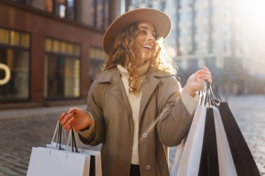 Alışveriş çantalı mutlu turist kadın Avrupa 'nın güneşli sokaklarında yürüyor. Güzel bir kadın alışverişten sonra havanın tadını çıkarır. Tüketim, alışveriş. Etkin yaşam biçimi.