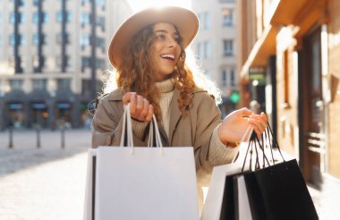 Alışveriş çantalı mutlu turist kadın Avrupa 'nın güneşli sokaklarında yürüyor. Güzel bir kadın alışverişten sonra havanın tadını çıkarır. Tüketim, alışveriş. Etkin yaşam biçimi.