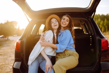 Araba yolculuğunda eğlenen, gülümseyen, sohbet eden, doğanın tadını çıkaran iki genç kadının portresi. Aktif yaşam tarzı, seyahat, turizm, doğa.
