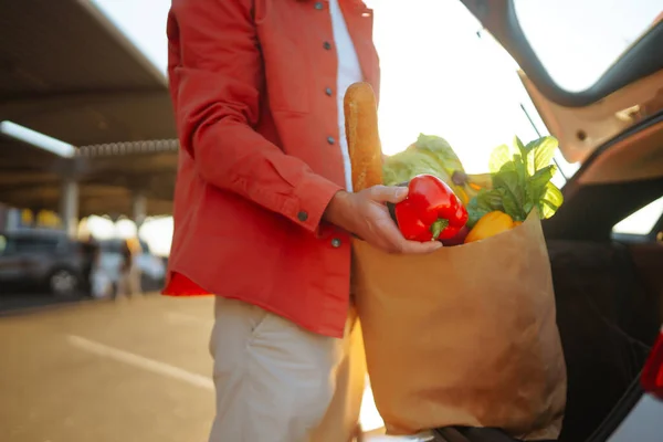 stock image Young man with a bag full of groceries, in a car. Grocery delivery man prepares fresh vegetable delivery service. Healthy lifestyle.