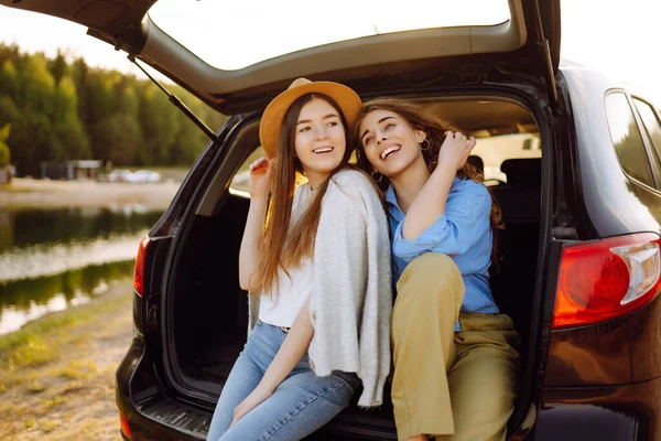 Portrait of two young women on a car trip having fun, smiling, chatting together, enjoying nature. Active lifestyle, travel, tourism, nature.