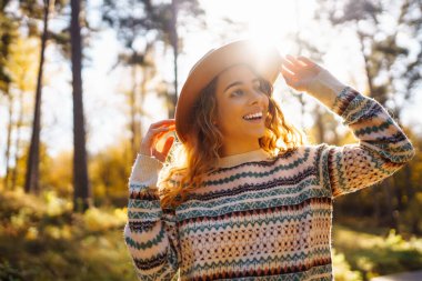 Şapkalı güzel genç bir kadın güneşli bir parkta sonbahar havasının tadını çıkarıyor. Moda, tarz kavramı. İnsanların konsepti, yaşam tarzı..