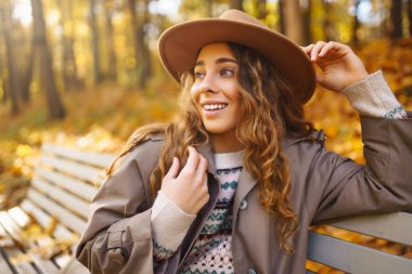 Şapkalı güzel genç bir kadın güneşli bir parkta sonbahar havasının tadını çıkarıyor. Moda, tarz kavramı. İnsanların konsepti, yaşam tarzı..