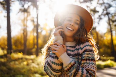Şapkalı güzel genç bir kadın güneşli bir parkta sonbahar havasının tadını çıkarıyor. Moda, tarz kavramı. İnsanların konsepti, yaşam tarzı..
