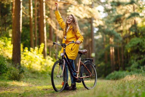 Sarı Ceketli Kıvırcık Saçlı Gülümseyen Kadın Güneşli Bir Parkta Bisiklet — Stok fotoğraf