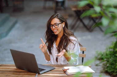 Modern bir kafede dizüstü bilgisayarla çalışan kablosuz kulaklıklı genç bir kadın ressamın portresi. Serbest çalışma kavramı, çevrimiçi eğitim, blog.