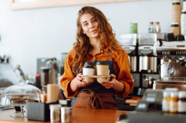 Gülümseyen bayan barista müşterilere kahve veriyor. Tezgahın arkasında kıvırcık saçlı bir kahve dükkanı sahibi çalışıyor. İş konsepti. Paket yemek.