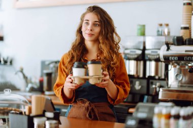 Gülümseyen bayan barista müşterilere kahve veriyor. Tezgahın arkasında kıvırcık saçlı bir kahve dükkanı sahibi çalışıyor. İş konsepti. Paket yemek.