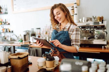 Başarılı küçük işletme sahibi dijital tabletle kahve dükkanının arkasında duruyor ve düzeni sağlıyor. Güzel kadın baristanın portresi. Satıcı-girişimci iş konsepti