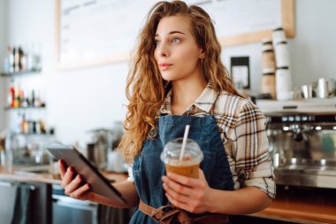 Başarılı küçük işletme sahibi dijital tabletle kahve dükkanının arkasında duruyor ve düzeni sağlıyor. Güzel kadın baristanın portresi. Satıcı-girişimci iş konsepti