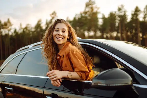 快乐的卷曲的女人笑着从车窗里探出头来享受大自然 在开阔的路上有一种自由的感觉美与旅行的概念 积极的生活方式 — 图库照片