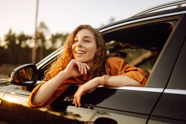 快乐的卷曲的女人笑着从车窗里探出头来享受大自然 在开阔的路上有一种自由的感觉美与旅行的概念 积极的生活方式 — 图库照片