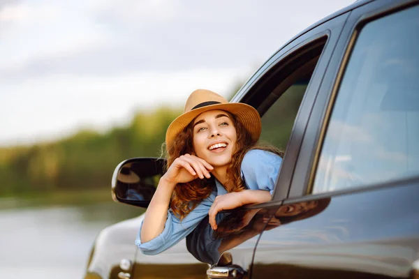 快乐的女旅行家 戴着帽子 享受着车窗上的夕阳西下 汽车旅行 — 图库照片