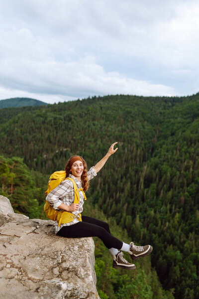 Beautiful woman with backpack admires view from top of mountain. Mountain tourism. Girl traveler on background of mountains. Active lifestyle.