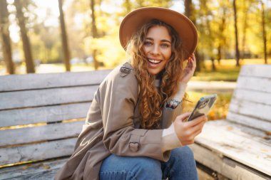 Güneşli sonbahar parkında akıllı telefonlu mutlu bir kadının portresi. Kadınlar telefonda konuşurken doğanın tadını çıkarırlar. Rahatlama, dinlenme kavramı