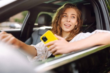 Şık bir kadın araba kullanıyor ve cep telefonu kullanıyor. Şehri dolaştım, park için yas tuttum. İş, teknoloji kavramı.