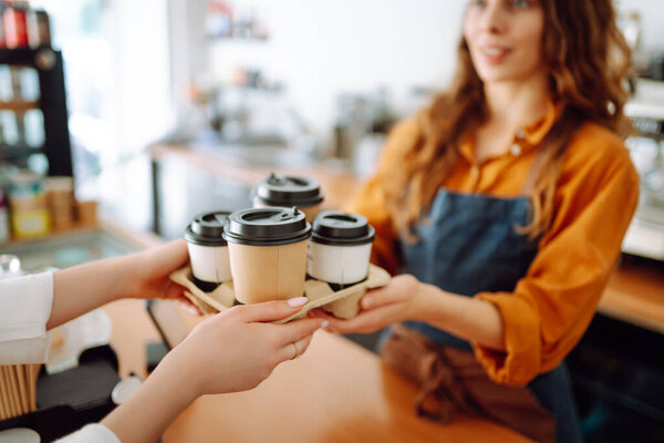 Beautiful barista woman issues coffee orders to go in a coffee shop. Small business owner. Takeaway food and drinks.