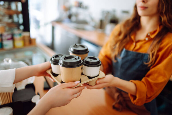 Beautiful barista woman issues coffee orders to go in a coffee shop. Small business owner. Takeaway food and drinks.