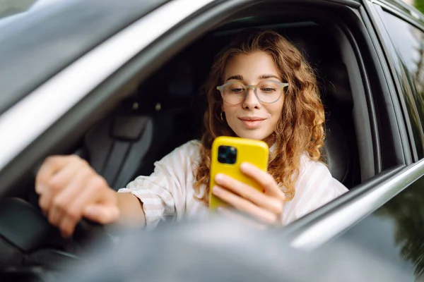 Şık bir kadın araba kullanıyor ve cep telefonu kullanıyor. Şehri dolaştım, park için yas tuttum. İş, teknoloji kavramı.