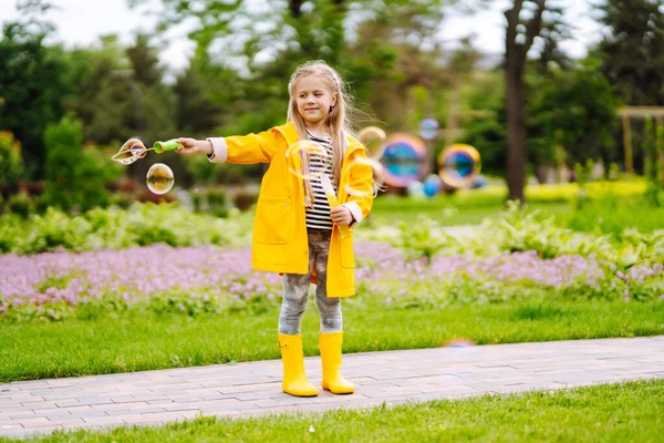 노란색 비옷을 쾌활한 소녀는 거품을 가을에 공원에서 산책을합니다 — 스톡 사진