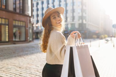 Güneşli bir günde Avrupa sokaklarında elinde alışveriş poşetleri olan şapkalı, güler yüzlü şık bir kadın yürüyor. Tüketim, alım, satış. Yaşam biçimi.