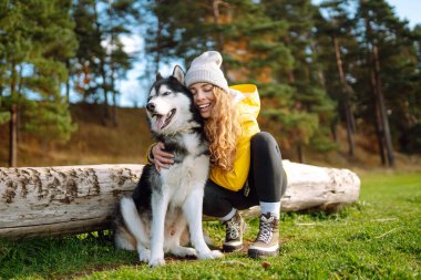 Şapkalı ve sarı paltolu güzel genç bir kadın parktaki çimlerde köpeğiyle yürüyor. Köpeğiyle dışarıda poz veren mutlu bir kadın. Arkadaşlık kavramı, tatil, yürüyüş.
