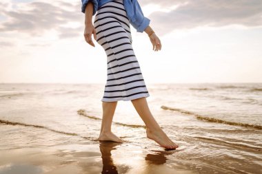 Sahilde deniz suyu ve kum dalgası üzerinde yürüyen genç bir kadının bacakları. Tatil, seyahat, özgürlük kavramı..